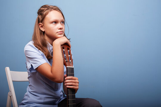 an 11-year-old girl is practicing a melody on a guitar on a blue background