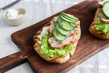 Sandwiches with chicken meat, cucumber, lettuce  and soft cheese on wooden board. Selective focus