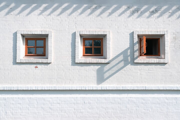 Three square windows in a row. The rightmost window is wide open. White brick wall with border