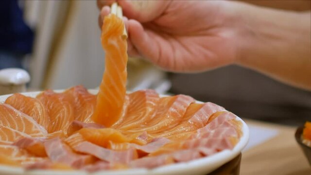 4k video of using chopctick pick slamon up from plate full of salmon sashimi, raw fish Japanese style food.