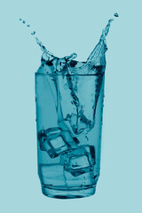 A blue summer drink splashed our of glass on blue background.