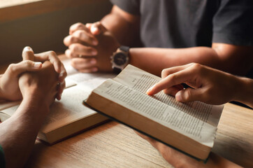 young man reading bible with friends who are praying to God Join the cell group at the church. A...