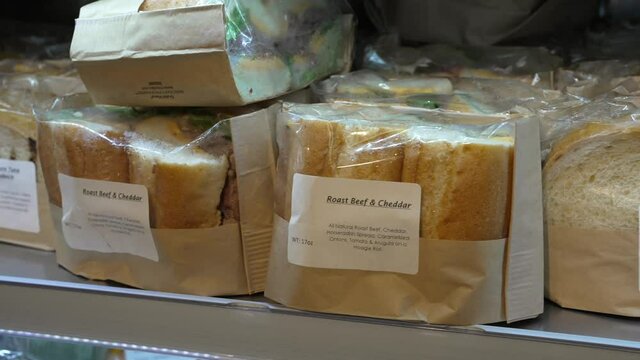 This panning video shows a display at a convenient market of rows of pre-packaged deli sandwiches.