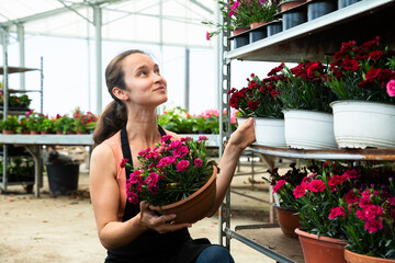 Friendly female gardener demonstrating garden flowers in flowerpots at garden store