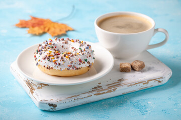 Fresh donut with cup of coffee and fall maple leaf. Autumn concept