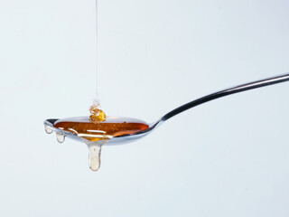 Honey dripping from metal spoon on white background