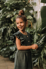 The face of a little girl surrounded by tropical leaves. Closeup portrait of a beautiful swarthy baby with perfect skin and dark hair. Natural cosmetics, health, cleanliness, skin care, beauty concept