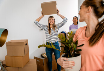 Three female friends carrying boxes into new home.