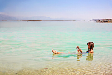 Girl with book is relaxing floating and swimming in the water of the Dead Sea in Israel. Recreation...