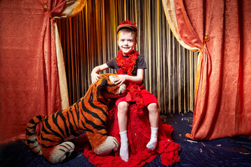 Yound boy during a stylized theatrical circus photo shoot in a beautiful red location. Models small...