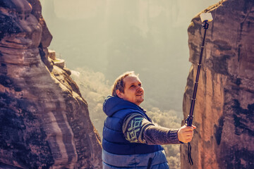 A man makes selfie on action camera on a cliff. A young guy is photographed on a rock after hiking in the mountains. Meteora, Greece