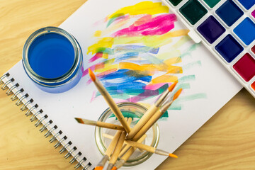 watercolor paints a jar of water and a jar with brushes on an album sheet with paint samples