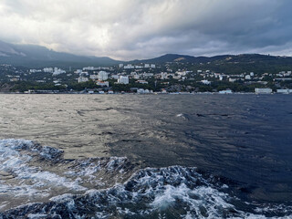 beautiful landscape where on the horizon behind the black sea with waves you can see the Crimean city in the mountains
