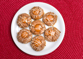 Three brown cookies with hazelnuts and peanut brittle on a brown transparent plate, caramel cream. White plate on red background