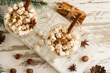 chocolate drink or cocoa with marshmallow in glass mugs on a white wooden table. top view of the drink cinnamon sticks, nuts, anise stars.