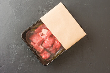 portioned pieces of fresh meat in vacuum packaging on a black background. top view. logo layout...