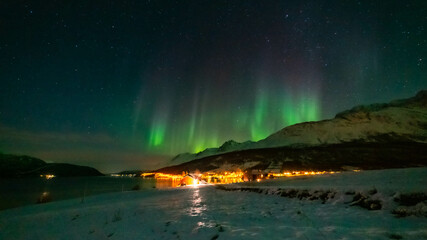 Nordlichter wie eine Krone über Lakselvbukt in den Lyngenalps, Norwegen. Aurora Borealis over snowy mountains. village on illuminated night