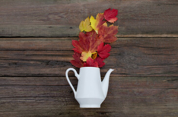 wooden background with teapot and autumn foliage. autumn bouquet of leaves on old background