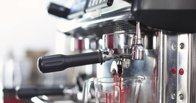Barista using finger press on start button to make cup of coffee and waiting while black drops of hot coffee fall to glass cup and take it away.