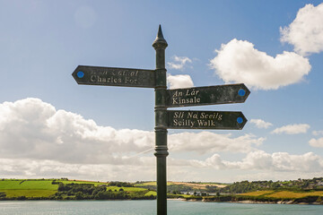 Old weathered sign with directions arrow to Fort Charles, Kinsale and Scilly walk. Cloudy sky in the background. County Cork, Ireland. Tourist information and direction.