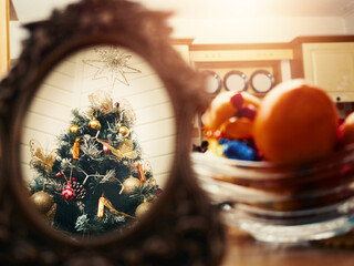 Christmas tree reflection in a mirror, bowl with fruits and sweets on a table. Festive season decoration abstract background. Muted colors. Double picture effect