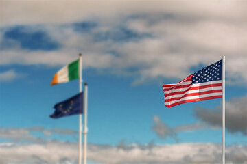 Waving flag of United States of America against pastel light blue color sky in focus. National flag of Ireland and Euro Union out of focus