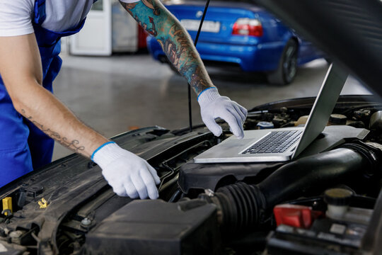 Repairman professional technician car mechanic man male hands in gloves use laptop pc computer make do diagnostics check fix problem with raised hood bonnet work in vehicle repair shop workshop inside