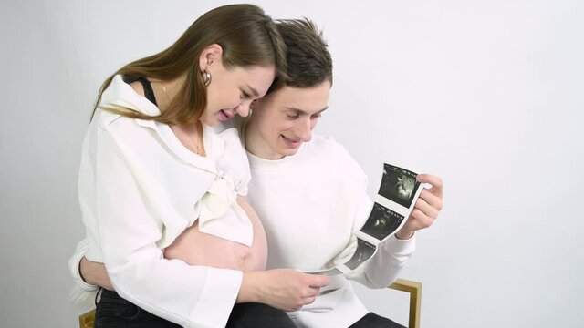 Young beautiful pregnant woman showing an ultrasound image to her husband. A couple in love is expecting a baby