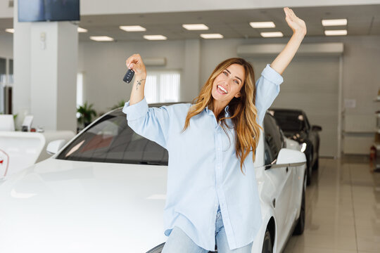 Happy cool woman customer female buyer client in blue shirt show keys stretch hand choose auto want buy new automobile in car showroom vehicle salon dealership store motor show indoor. Sales concept.