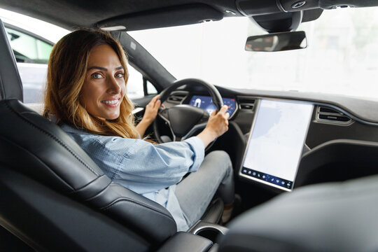 Back view happy caucasian smiling confident satisfied woman drive hold put hand on steering wheel using maps on tablet look camera sit in auto new car automobile Journey traveling lifestyle concept.