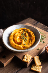 Bowl with pumpkin hummus, delicious appetizer decorated with greens and spices