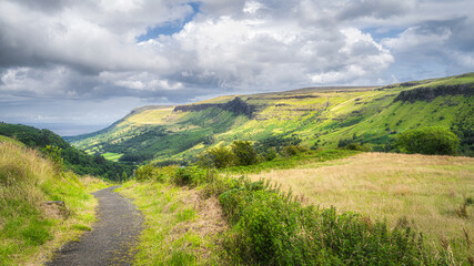 Fototapeta premium Trail or footpath in Glenariff Forest Park leading between hills to beautiful green valley, Antrim, Northern Ireland