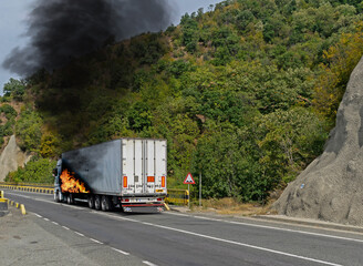 The freight truck caught fire at the entrance to a bridge. The truck is burning.