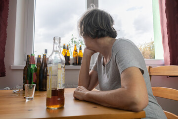 old senior female woman sit next to table drink alcohol bottle at home sad alone alcoholism Signs...