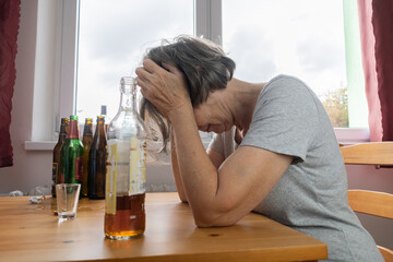 old senior female woman sit next to table drink alcohol bottle at home sad alone alcoholism Signs...