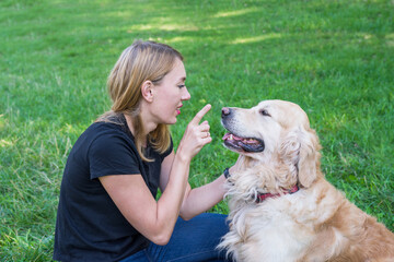 Young woman playing with her dog retriever touching the dog's nose while lying on the grass in the park.