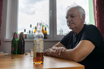 old senior male man sit next to table drink alcohol bottle at home sad alone alcoholism Signs and...