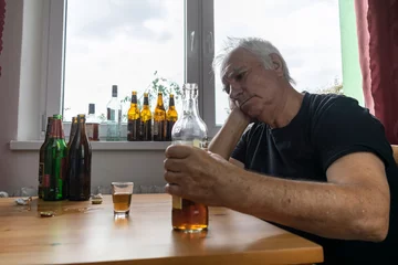 Gordijnen old senior male man sit next to table drink alcohol bottle at home sad alone alcoholism Signs and Symptoms rehab abuse and recovery problems © kirill