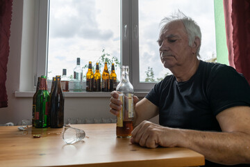 old senior male man sit next to table drink alcohol bottle at home sad alone alcoholism Signs and...