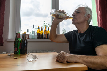 old senior male man sit next to table drink alcohol bottle at home sad alone alcoholism Signs and...