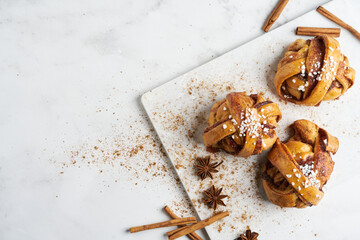 Fresh vegan cinnamon buns on marble board and white marble table