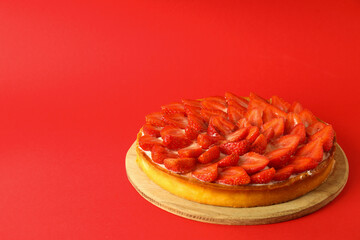 Round board with strawberry tart on red background