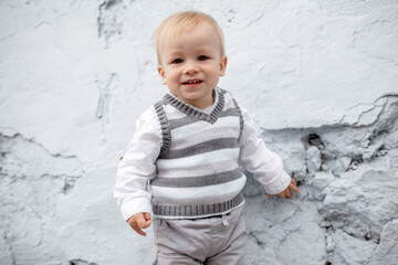 Fototapeta premium Stylish male toddler dressed fashion clothes, grey jeans, sweater and walking against the street wall