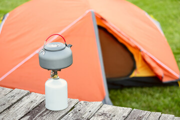 kettle on a gas burner with orange tent in a camping site. The stove is used for more eco-friendly...
