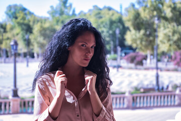 Middle-aged adult Hispanic woman with black curly hair, sensual holding the collar of her suit. Fashion concept, sensuality, sensations, looks.