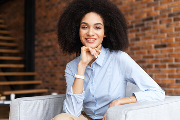 Headshot portrait of a charming elegant biracial woman with her hand on a chin, wearing shirt...