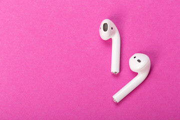 Modern wireless bluetooth headphones with charging case on pink background. The concept of modern...