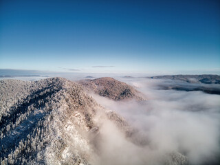 Aerial view, sea of fog and slope illuminated by the rising sun, snow on the tops of the mountains. Russia