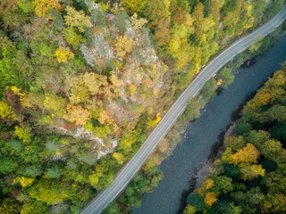 Aerial view of the road and colorful autumn forest with a mountain river in Russia, Adygea