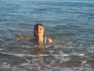 Portrait of a girl enjoying and relaxing in the ocean water. The concept of leisure, carelessness and relaxation. A young girl plays and swims in the waves on the sea on a sunny day